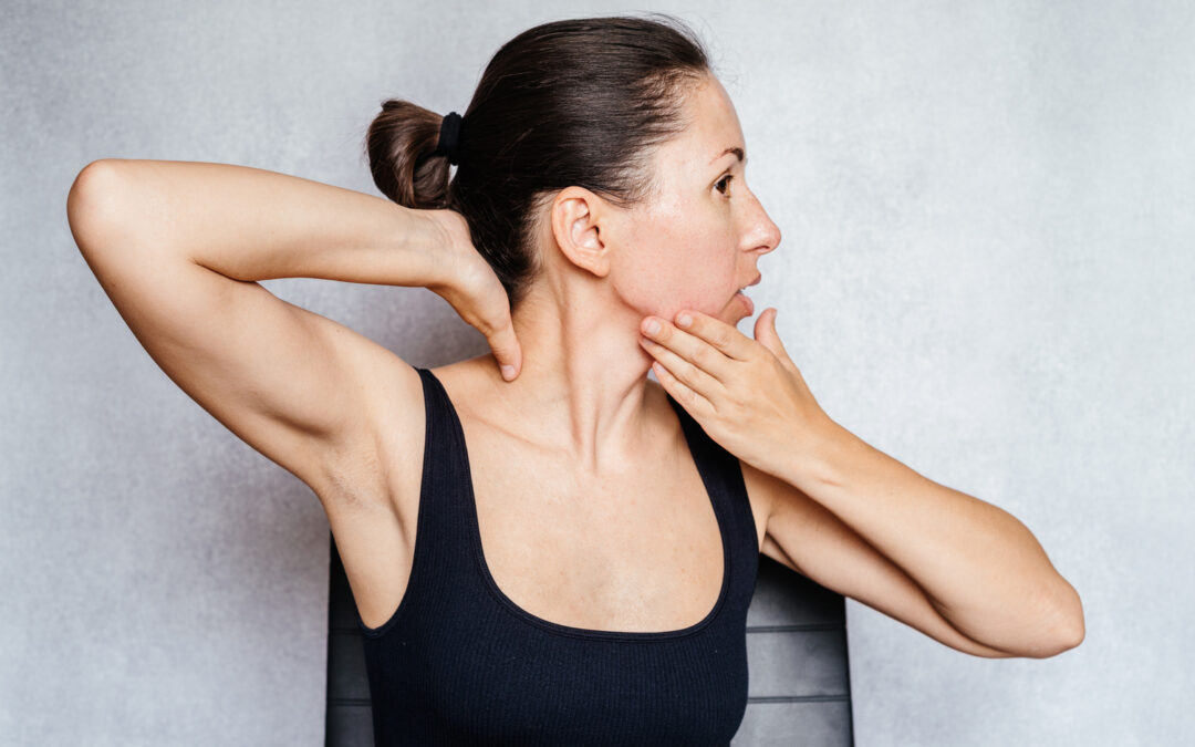 A woman gently rotates her head with both hands while doing the McKenzie method exercise for the neck pain
