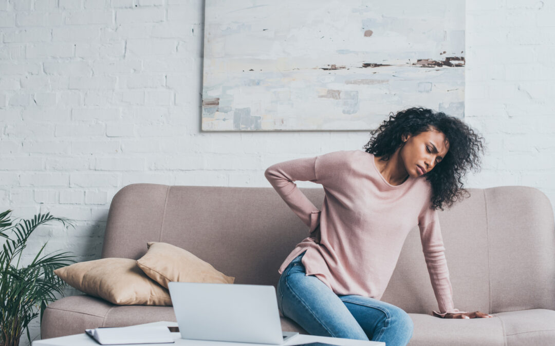 woman suffering from back pain while sitting on sofa